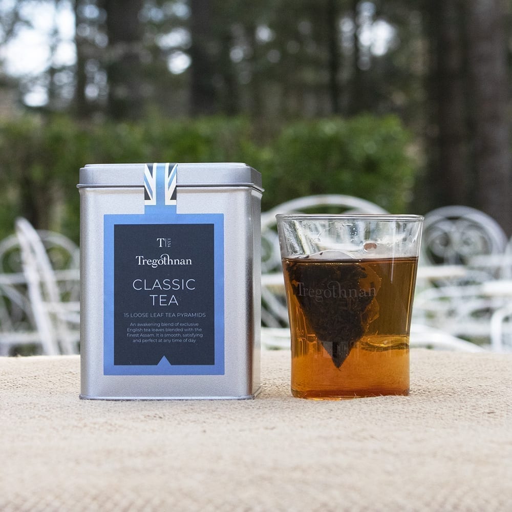 Tregothnan Classic Tea tin featuring loose leaf tea pyramids, a glass tea cup with tea inside,set against a blurred garden background